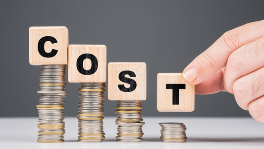 Visual representation of reducing costs: wooden blocks spelling 'COST' on decreasing coin stacks