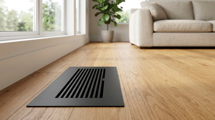 Matte black 4x10 aluminum floor register sitting flush in an oak hardwood floor by a living room window
