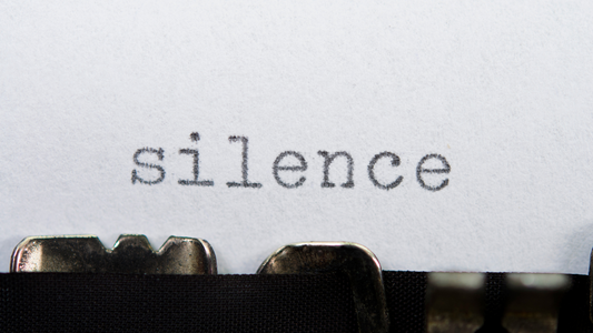The word “silence” typed on white paper using a typewriter ribbon, viewed in close-up.