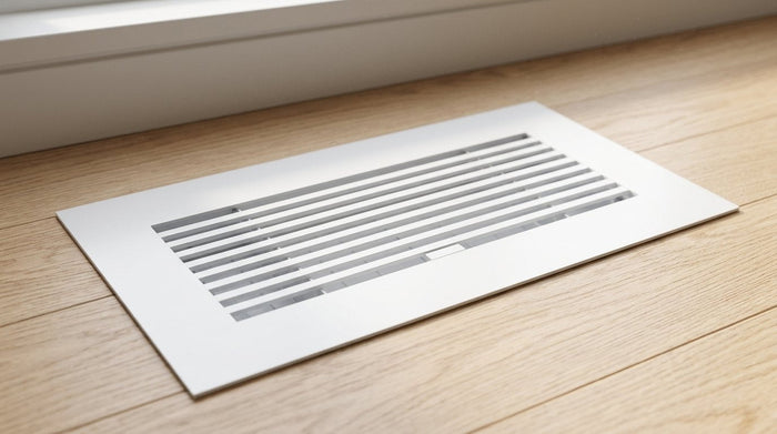 White aluminum floor register in a hardwood floor near a window
